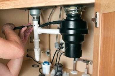 Plumber repairing a garbage disposal beneath a kitchen sink in Pottstown